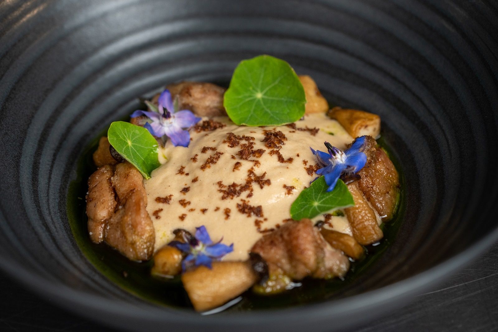 An elegant dish in a black bowl, decorated with edible flowers and green leaves.
