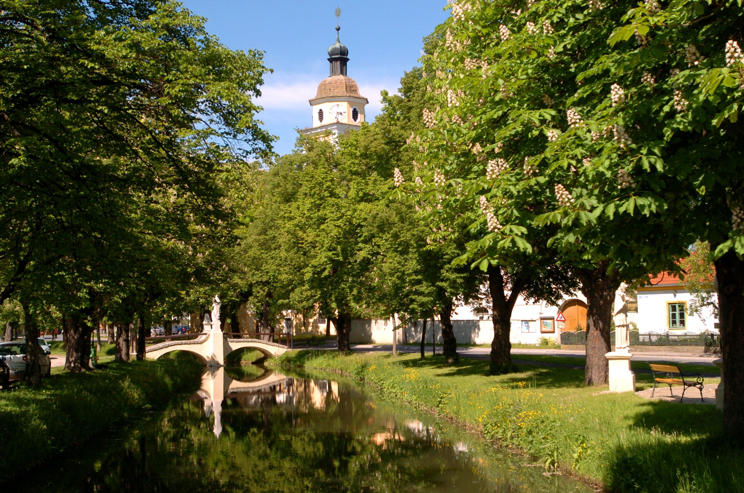 An idyllic park with a small river, a bridge and a church tower in the background.
