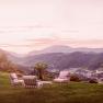 Garden furniture on a meadow with a view of a mountain landscape at sunset.