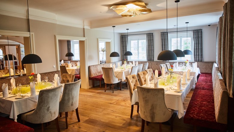Elegant restaurant with set tables, upholstered benches and hanging lamps at Schloss Luberegg