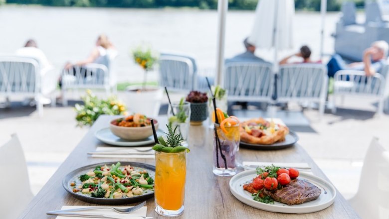A table with various dishes and drinks on the riverbank.