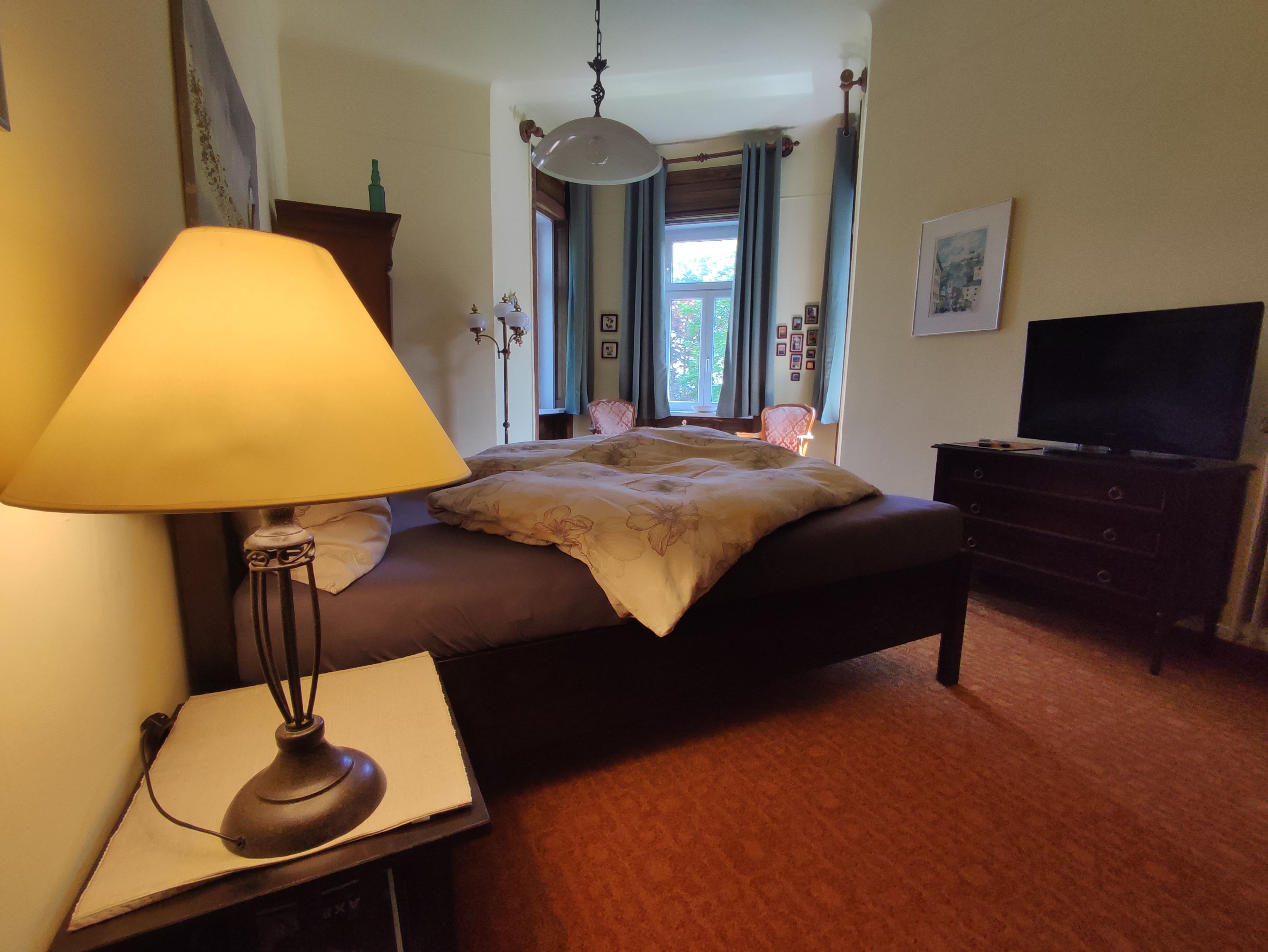 Comfortable bedroom with double bed, bedside lamp, window and TV.