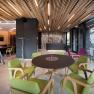 Interior view of a modern hotel lounge with wooden elements, green and purple chairs and a round table.