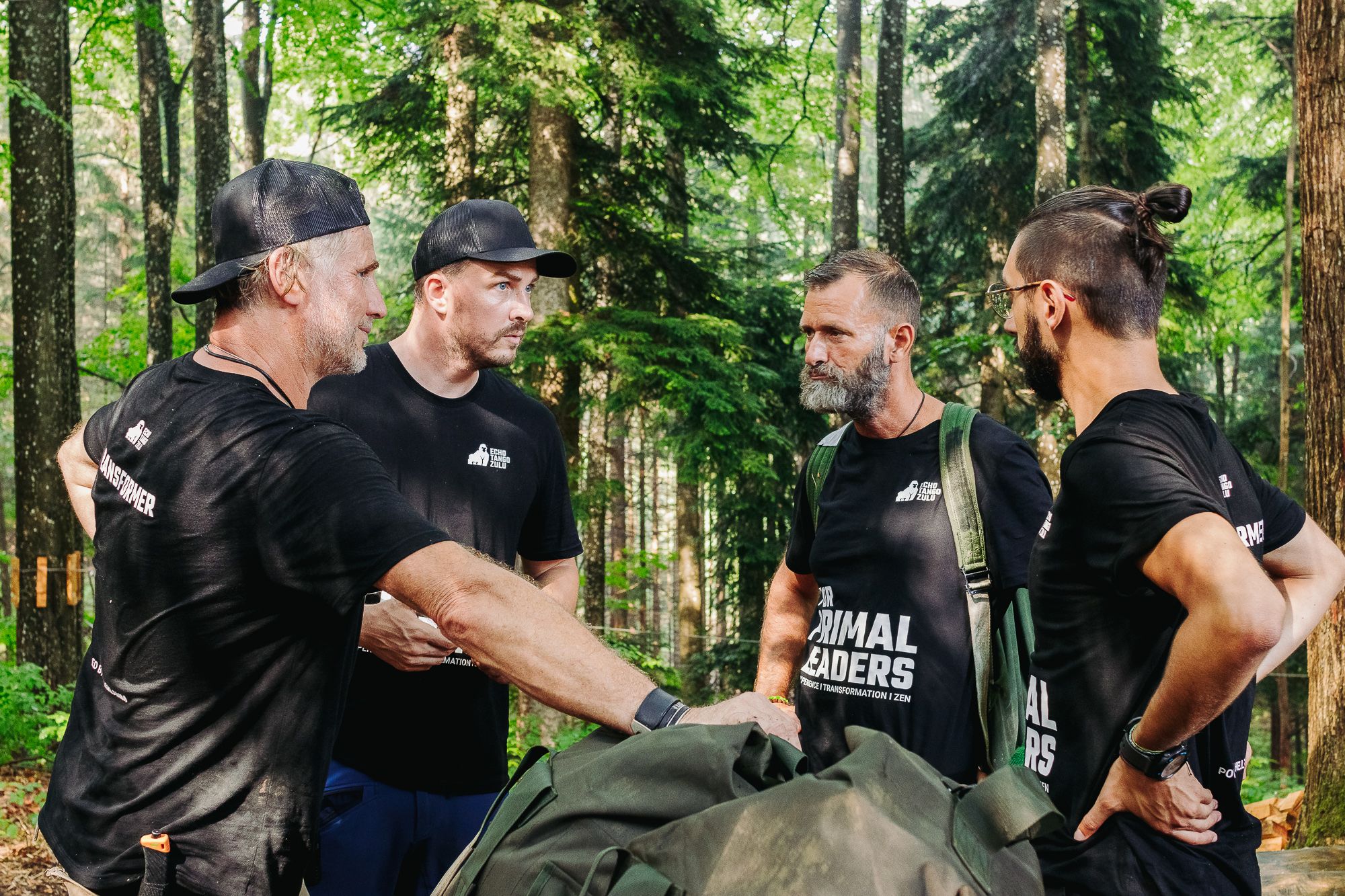 Four men in black T-shirts are standing in the forest and talking.