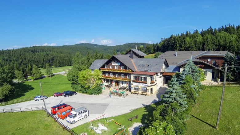 Alpengasthof Postl in a green, wooded landscape with several parked cars and a playground in the foreground.