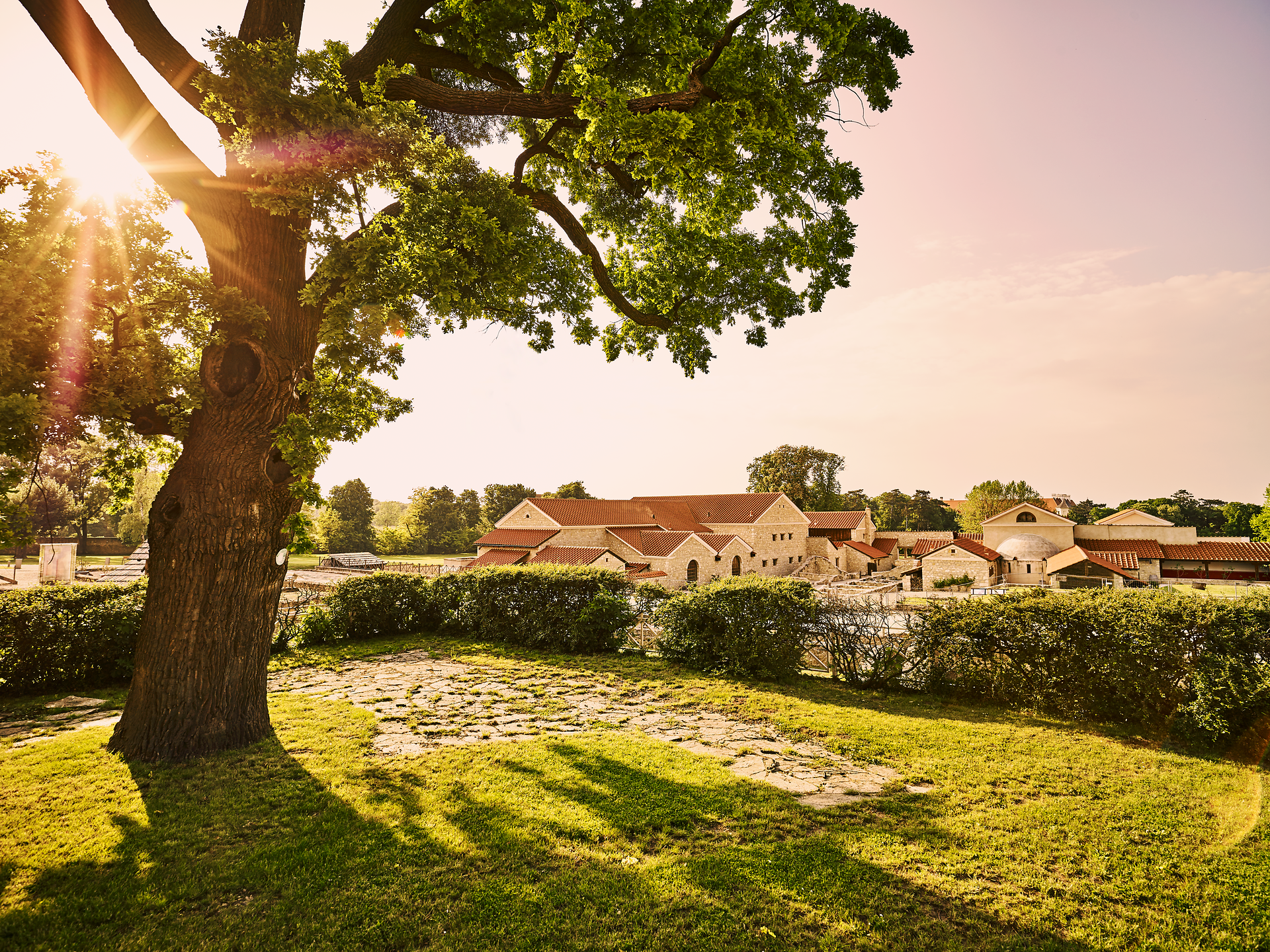 Roman town of Carnuntum with reconstructed buildings and red roofs, surrounded by green trees and lawns.