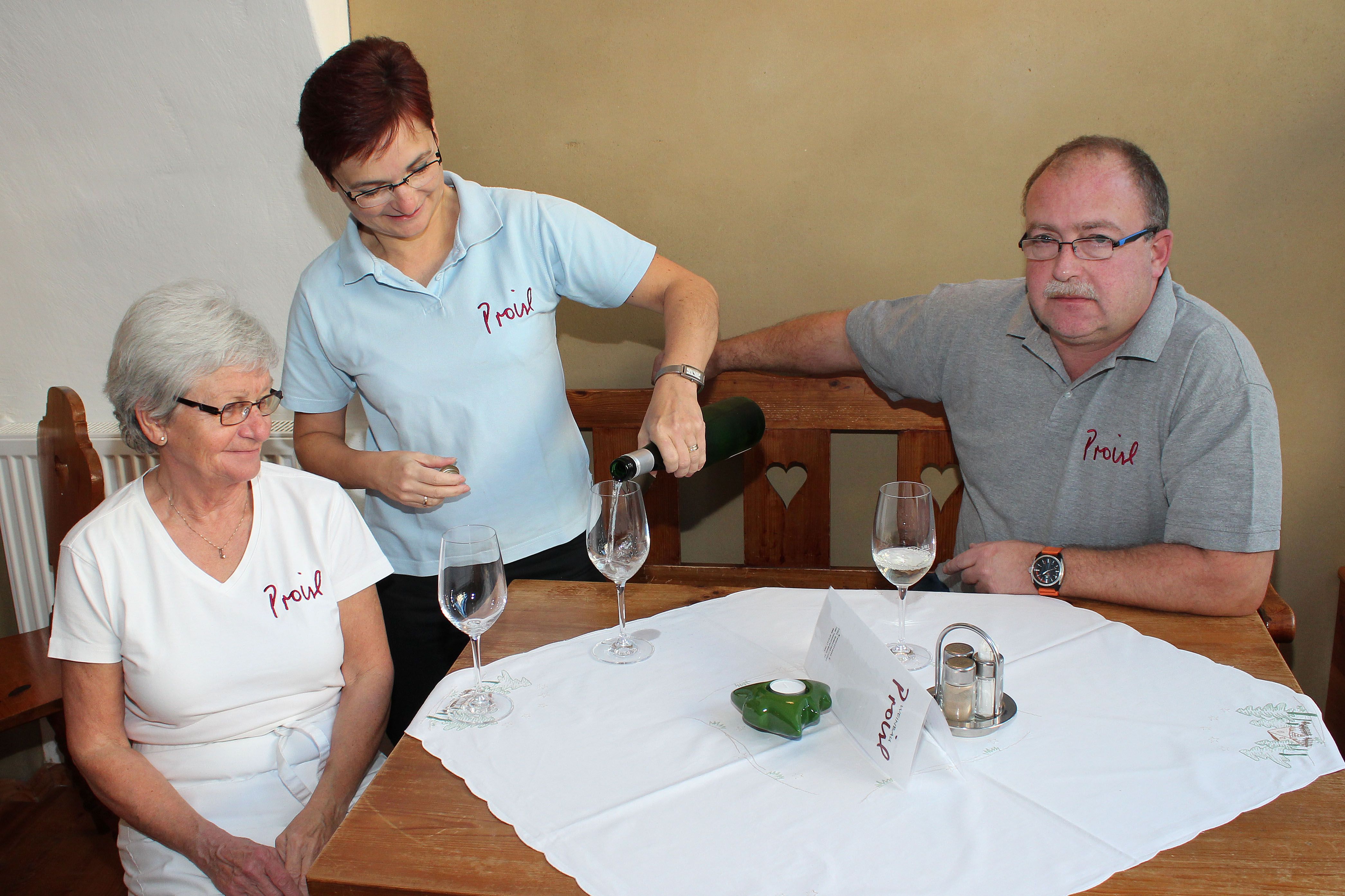 Three people are sitting at a table, a woman is pouring wine.