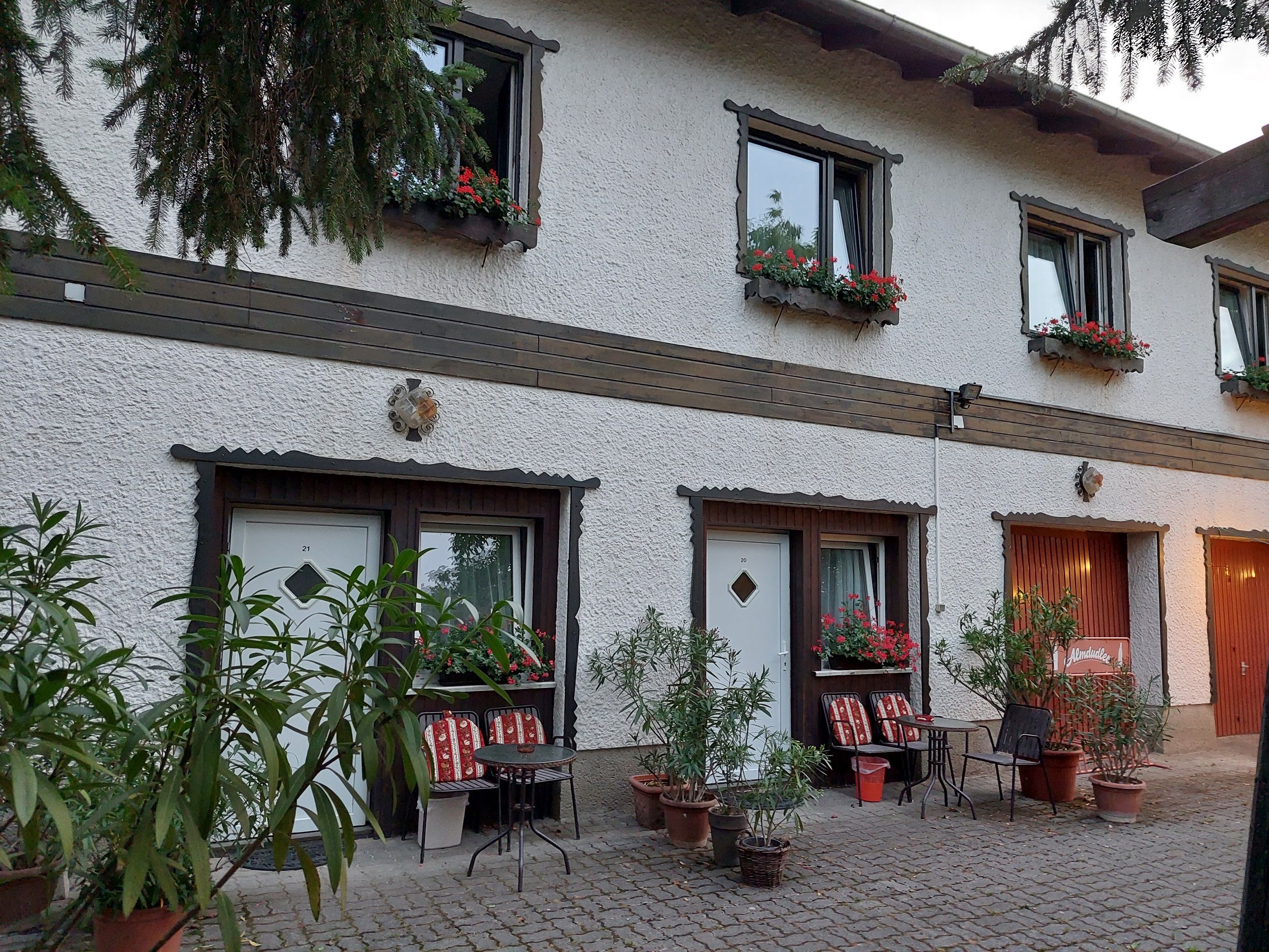 Exterior view of a two-story building with white walls, flower boxes and seating in front of the doors.