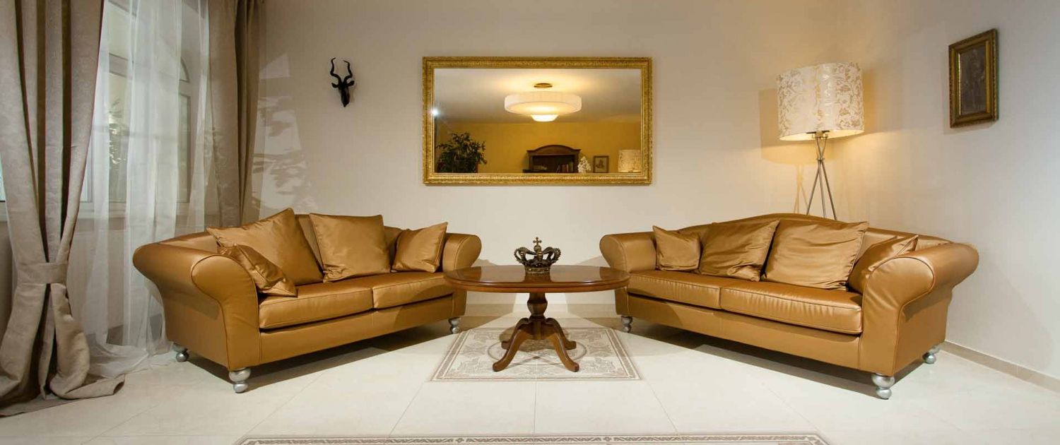 Elegant lobby with two brown sofas, a round wooden table and a large mirror on the wall.