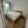 Bright bedroom with wooden floor, double bed and window with view of the greenery.
