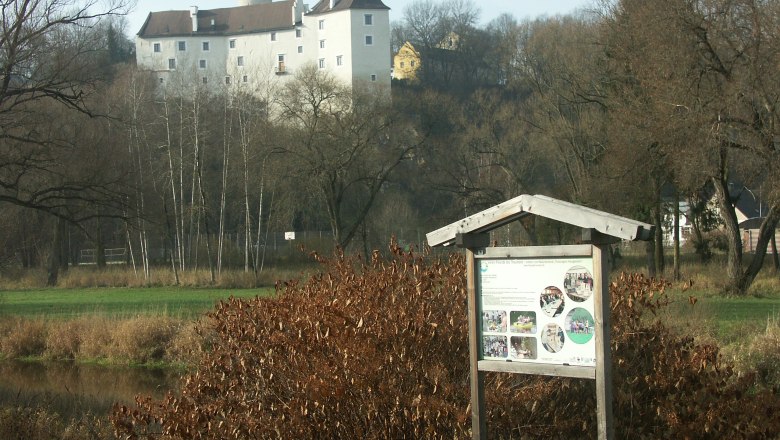 A nature trail sign in front of a castle in a rural landscape.