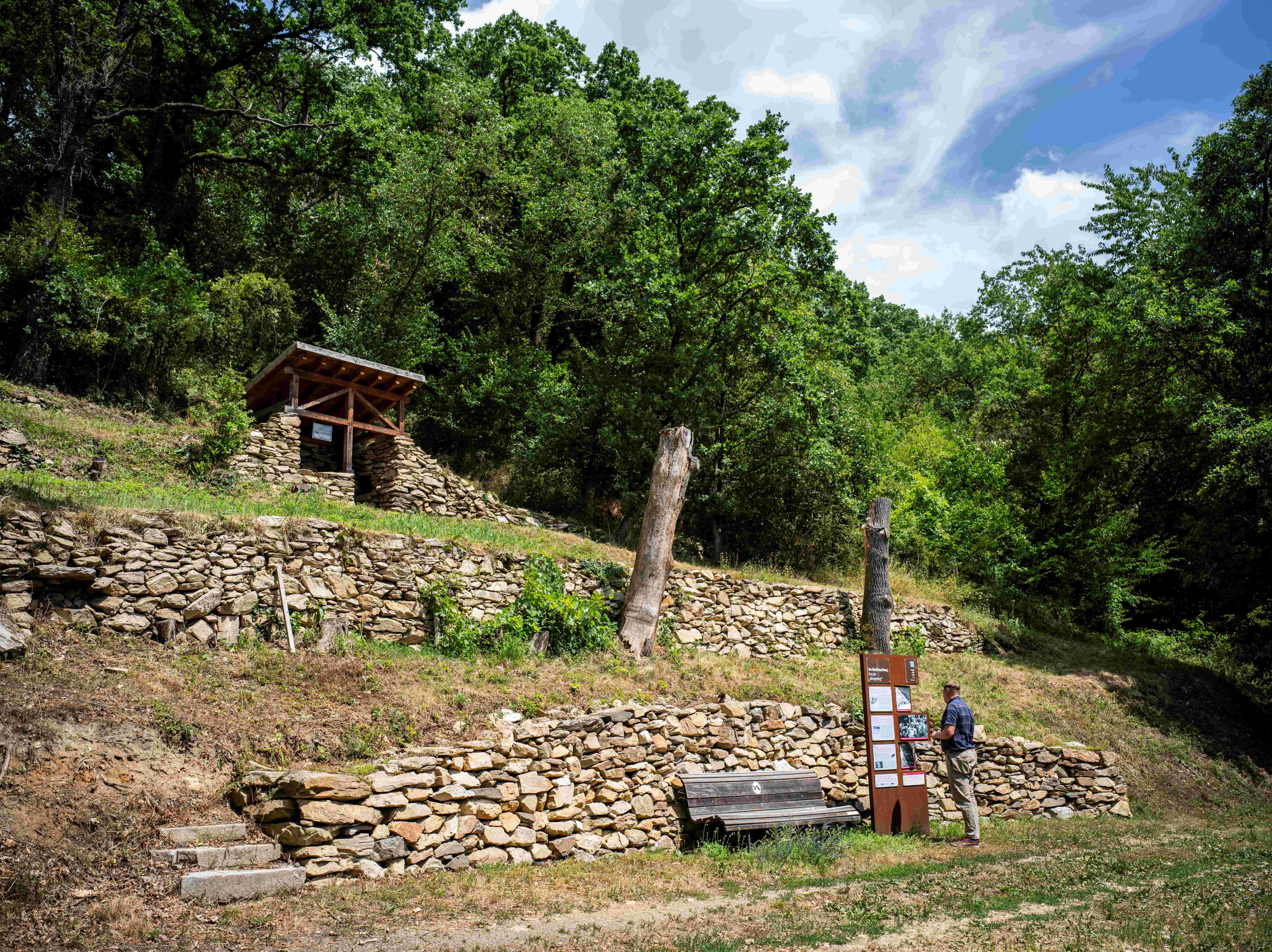 Stone walls and information board in a wooded area.