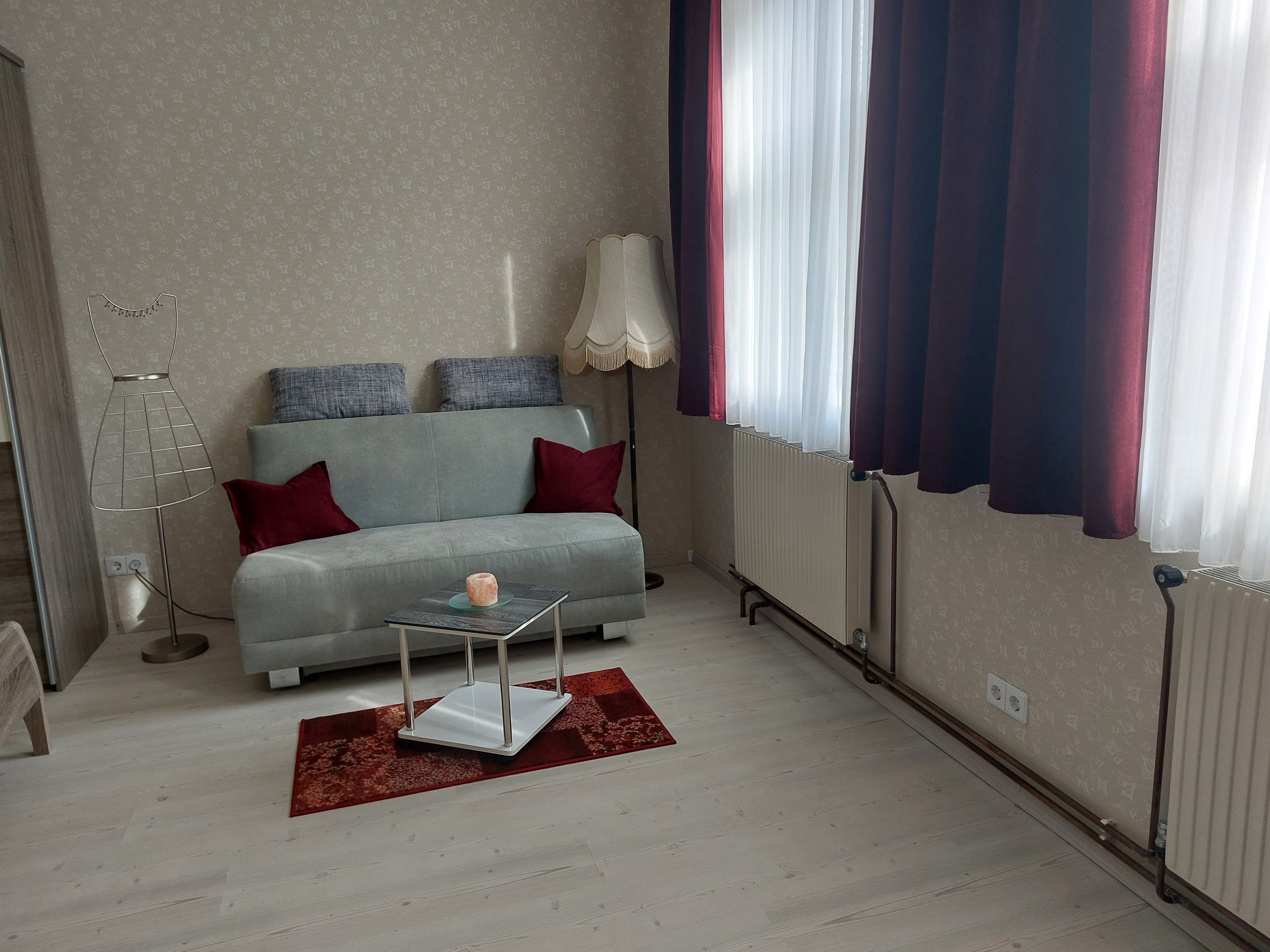 Living room with gray sofa, red cushions, floor lamp and small table on a red carpet.