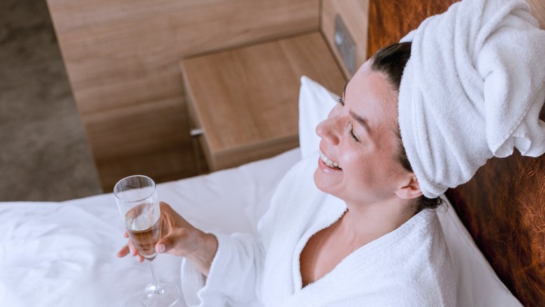 Two people in bathrobes have breakfast in bed with champagne and dessert.