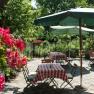 A cozy guest garden with red and white checkered tablecloths, green parasols and blooming flowers in the foreground.
