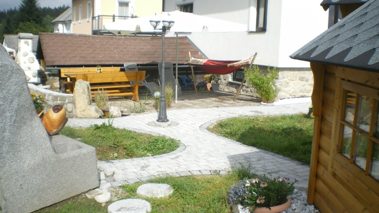 Garden with stones, wooden house, table, hammock and parasol.