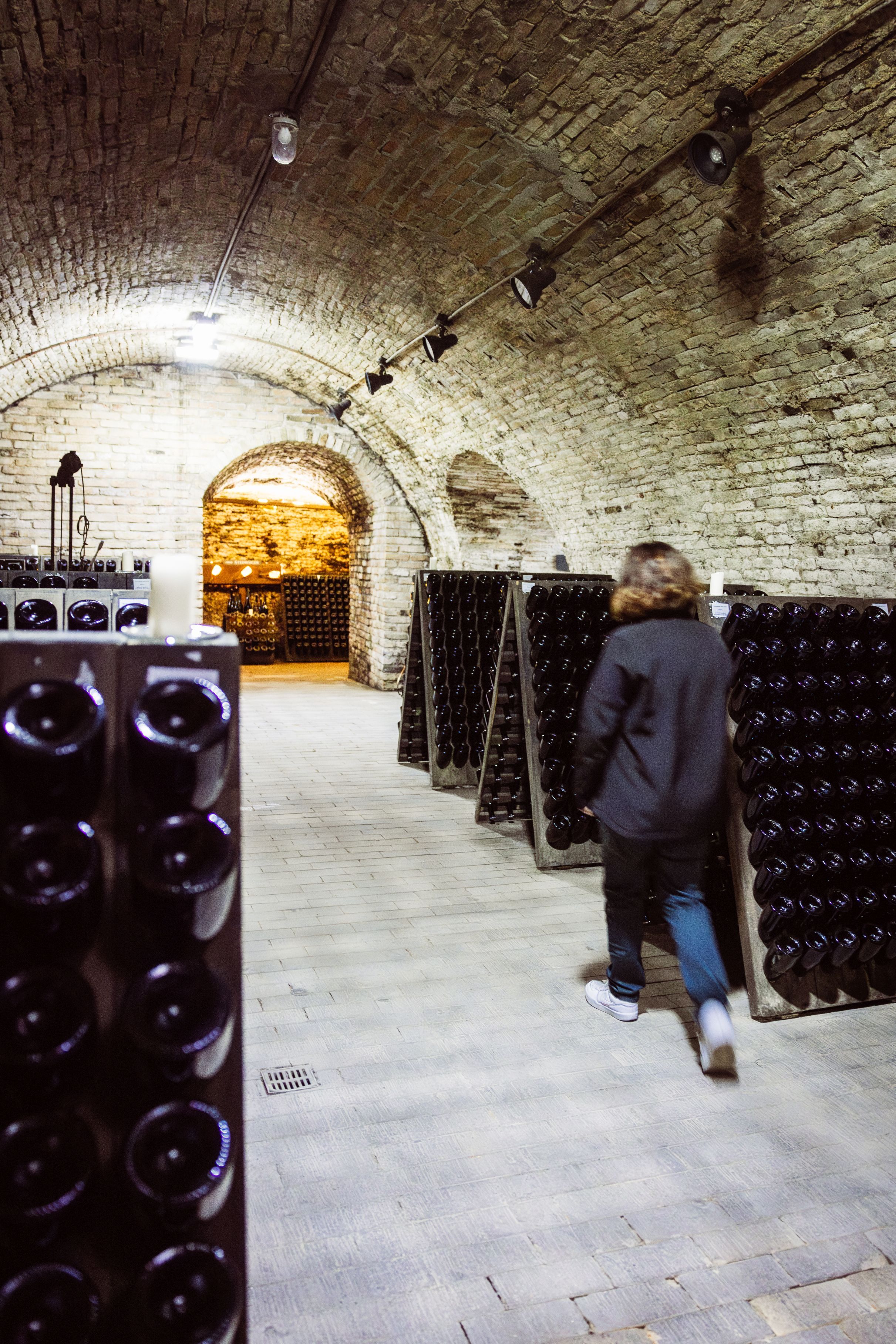A person walks through a historic wine cellar with sparkling wine racking tables and a vaulted brick ceiling at Steininger Weinwelt.