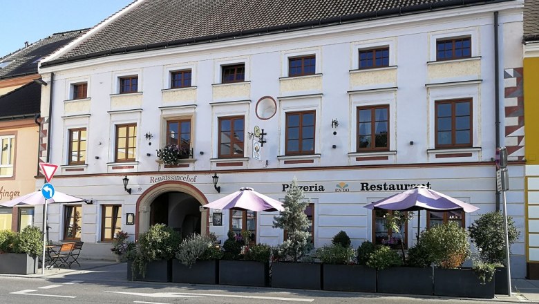 Historic building with pizzeria and restaurant, decorated with plants and parasols.