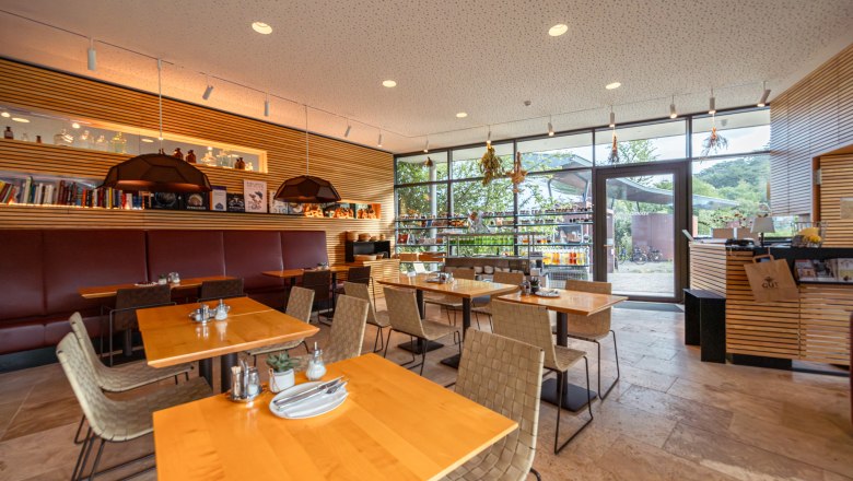 Interior view of a modern restaurant with wooden tables and large windows.