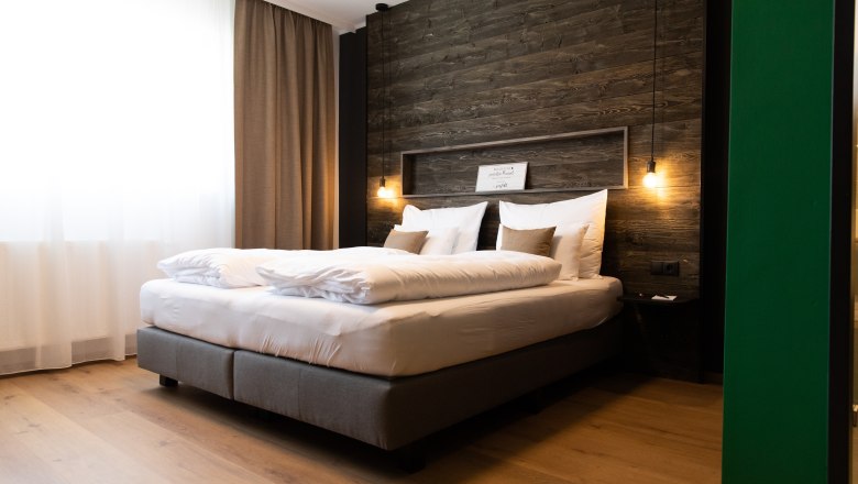 VinoQ, © ohida OG / ohne.media Modern hotel room with large bed, wooden wall and hanging lamps.