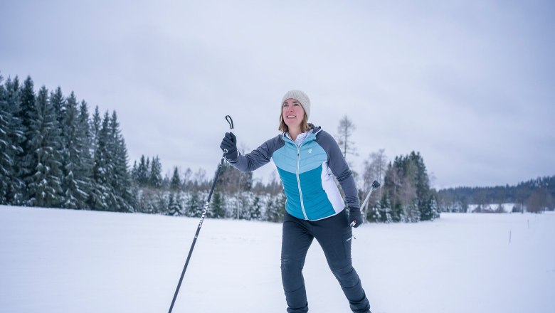 A woman cross-country skiing in a snowy landscape with trees in the background.