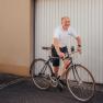 Man in white polo shirt rides bicycle in front of garage door.