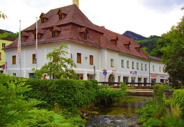 Pension Sun, © Pension Sun Historic building with a red roof by a stream, surrounded by green vegetation.