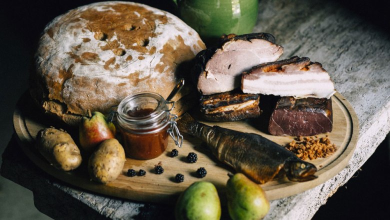 A rustic arrangement with bread, meat, fish, pears, potatoes and jam on a wooden table.