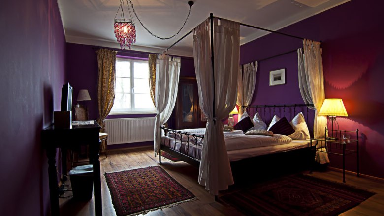 A cozy bedroom with a four-poster bed, purple walls and warm light.