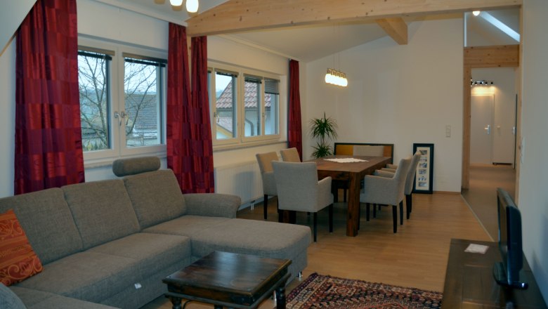Living room with gray sofa, wooden table and chairs, red curtains and ceiling lights.