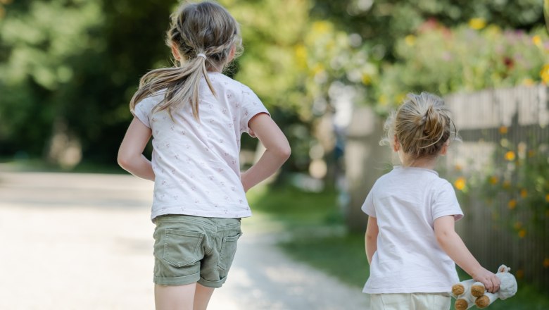 Two children running on a gravel path in a green park.