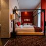 Elegant hotel room with four-poster bed, red accents and modern bathroom.