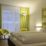 Modern hotel room with double bed, green-yellow curtains and wall decor.