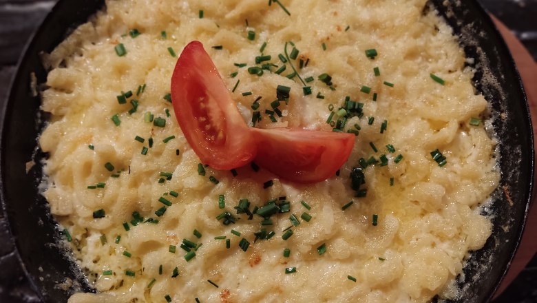 A pan of cheese spaetzle, garnished with tomatoes and chives.