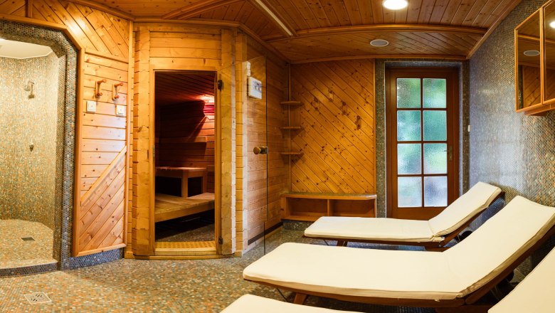 A cozy sauna area with wooden panelling, loungers and a shower.