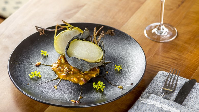 A dish of stone-crusted kohlrabi on bacon pear must jam, served on a black plate with yellow flowers.