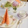 An elegantly laid table with flowers, orange dotted napkins and tableware with fruit motifs.