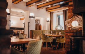 Cozy restaurant with wooden beams, green upholstered chairs and decorative lamps.