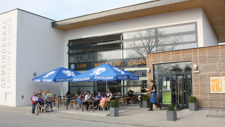 Exterior view of Cafe Adrienn with guests under blue parasols.