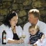 Family sitting at a table with wine bottles and glasses in front of a stone wall.