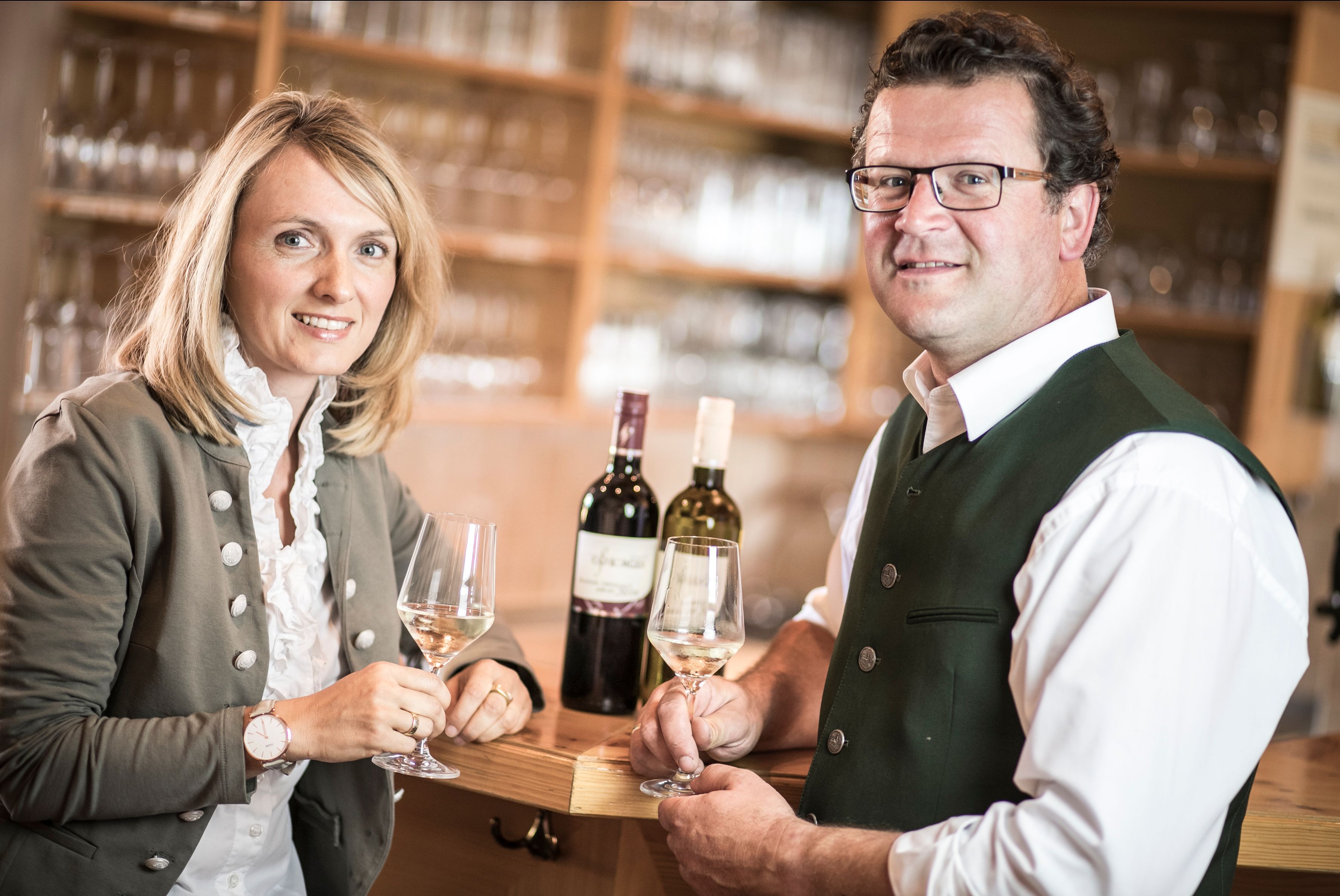 Two people in traditional dress holding wine glasses in a wine tavern.