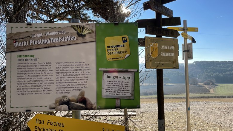Signpost and information board in a rural landscape with a blue sky.