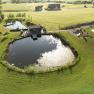 Aerial view of two ponds with surrounding grassland and a small building on the shore.
