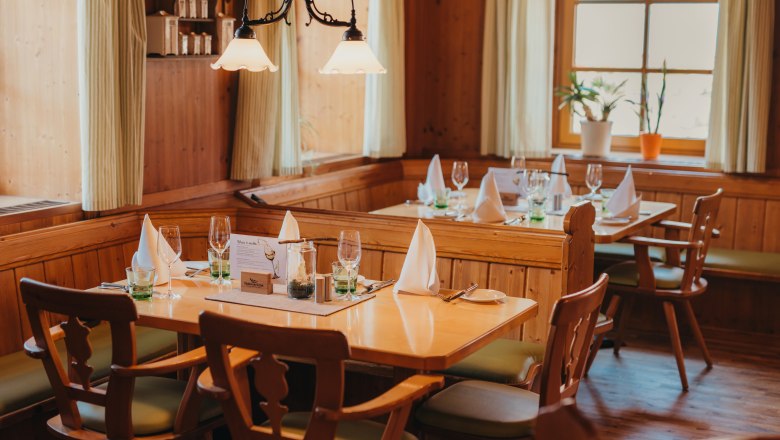 Cozy restaurant with wooden furniture, set tables and plants by the window.
