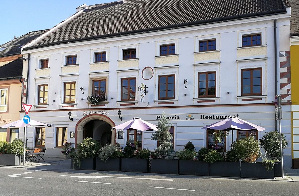 Historic building with pizzeria and restaurant, decorated with plants and parasols.