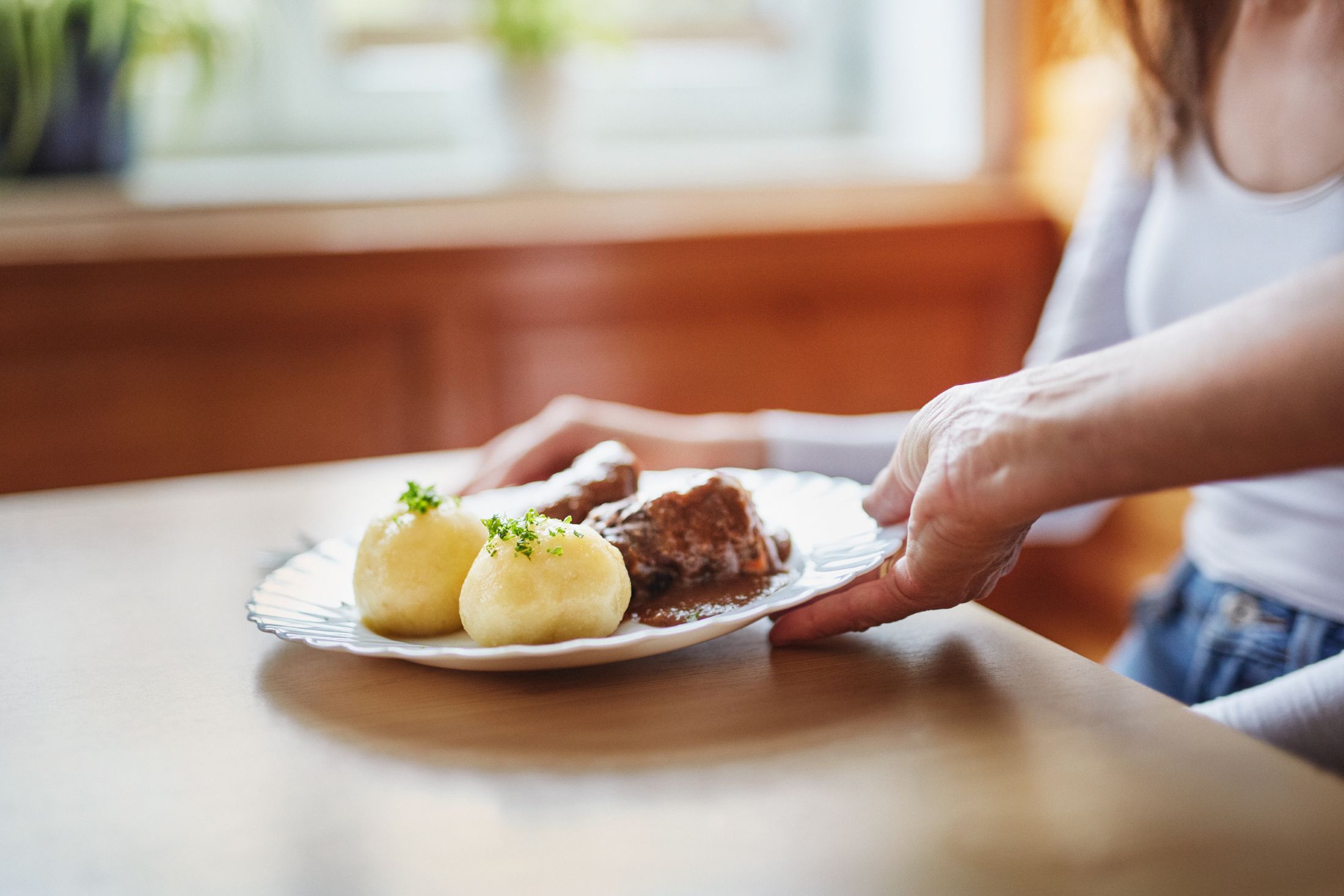 A plate with two Waldviertel potato dumplings and meat in sauce is served on a table.