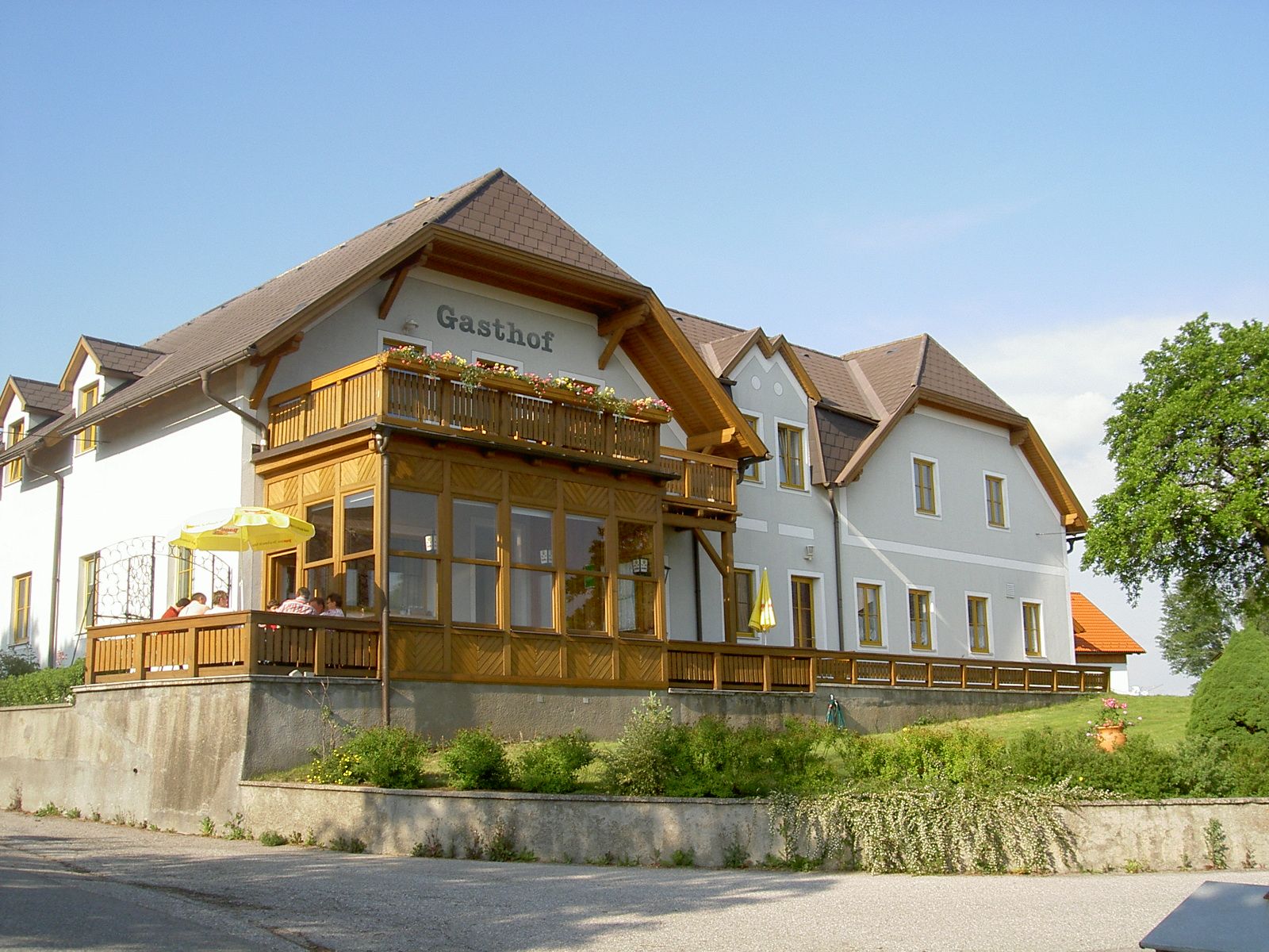 A traditional inn with a wooden veranda and flowers on the balcony, surrounded by green countryside.