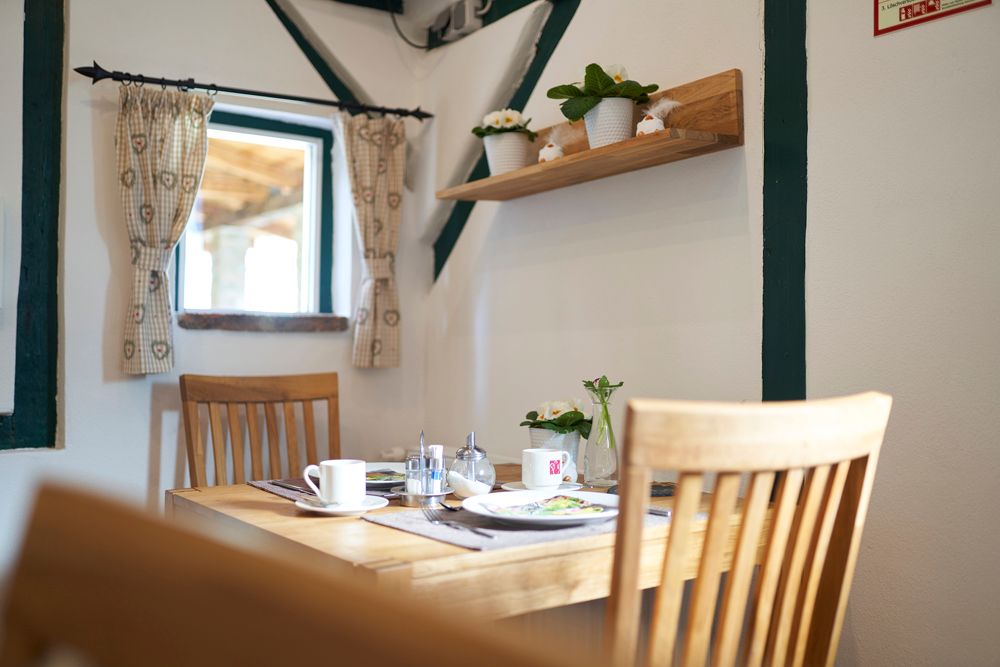 A cozy breakfast room with a wooden table, chairs and decorative plants on a shelf.