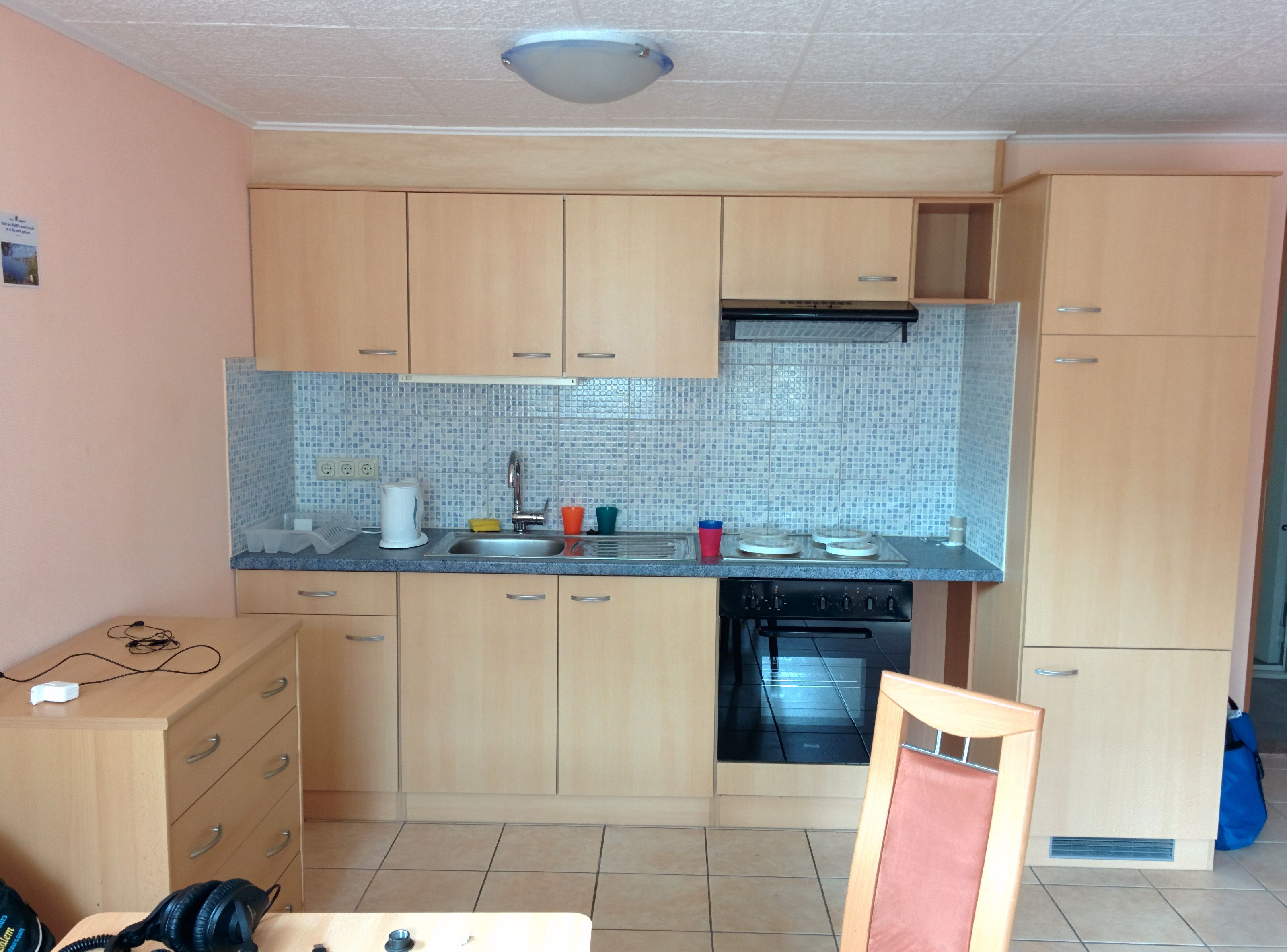 Small kitchen with wooden cupboards, sink, stove and tiled splashback.