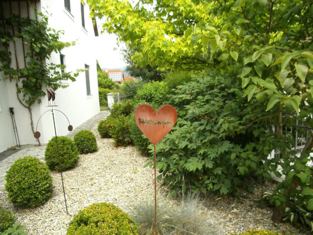 Garden with heart welcome sign and green bushes in front of a white building.